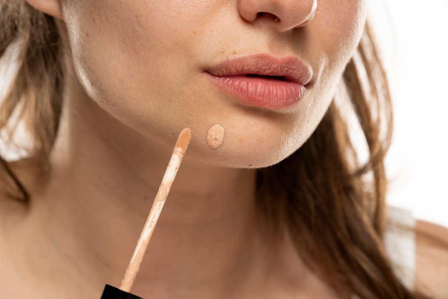 Frau trägt Concealer auf, um einen Pickel am Kinn abzudecken.
