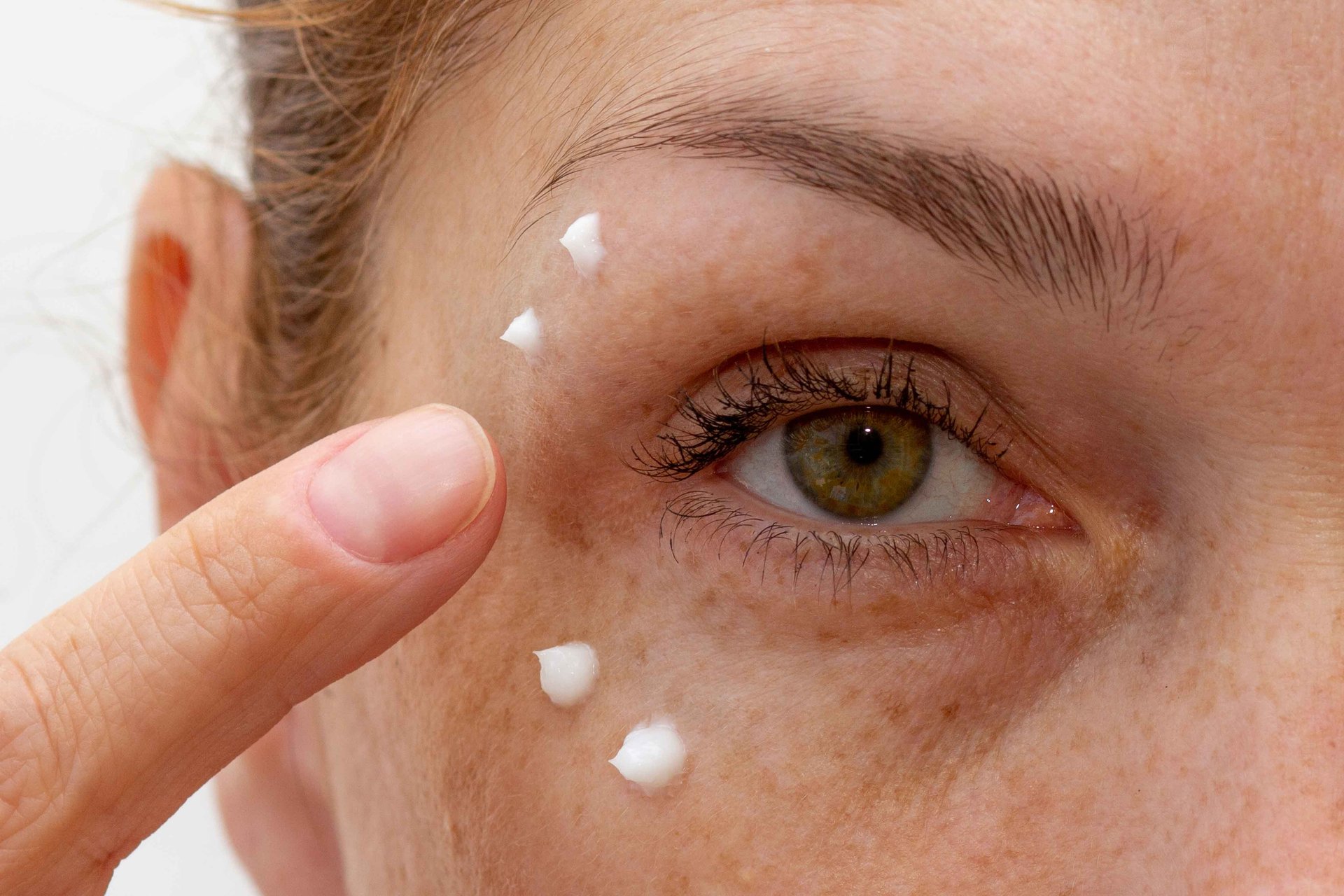 Eine Frau trägt mit ihrem Finger Creme um die Augen auf um Falten vorzubeugen