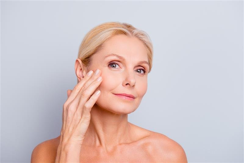 Mittelalte Frau berührt ihre Wange und zeigt glatte, gesund aussehende Haut.