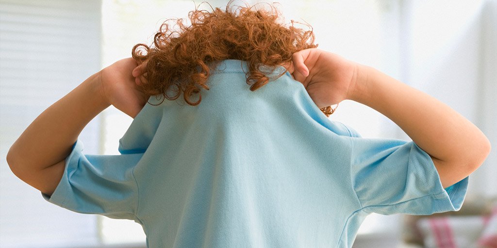 Kleidung bei Neurodermitis: Junges Kind zieht sich das T-Shirt über den Kopf