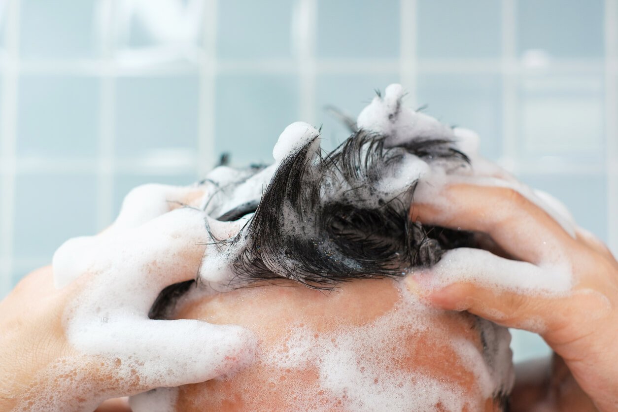 Mann schaeumt sich die Haare mit Shampoo ein