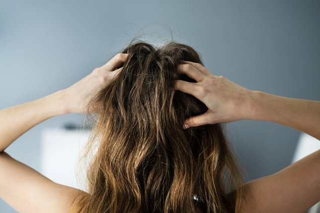 Der Kopf einer Frau mit dunklen Haaren von hinten, sie greift sich in die Haare.