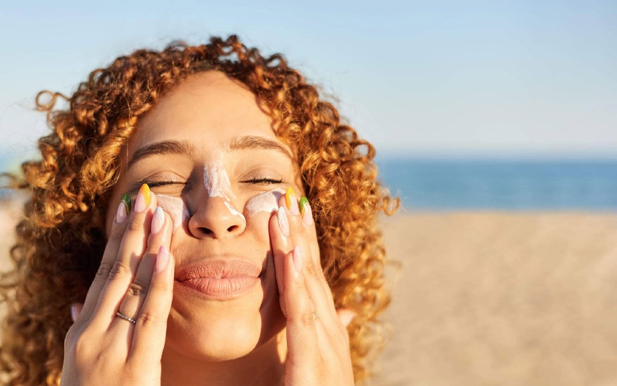 Frau trägt am Strand Sonnencreme auf Wangen und Nase auf