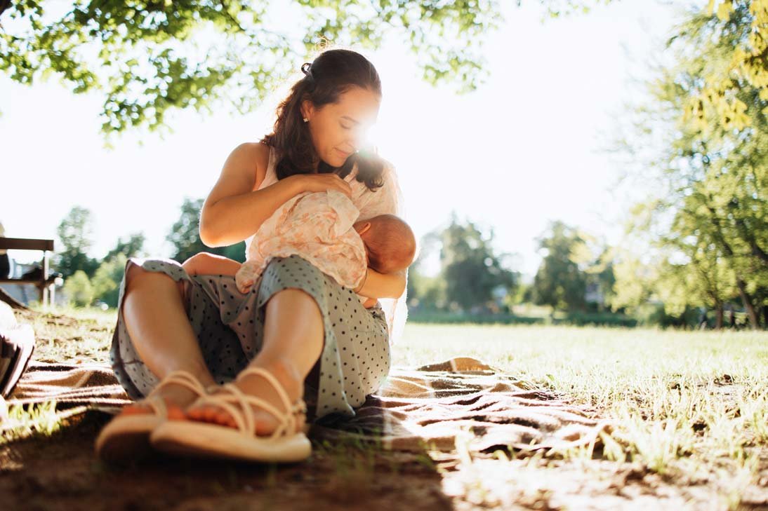 Mutter stillt ihr Baby auf einer Decke im Park bei sonnigem Wetter
