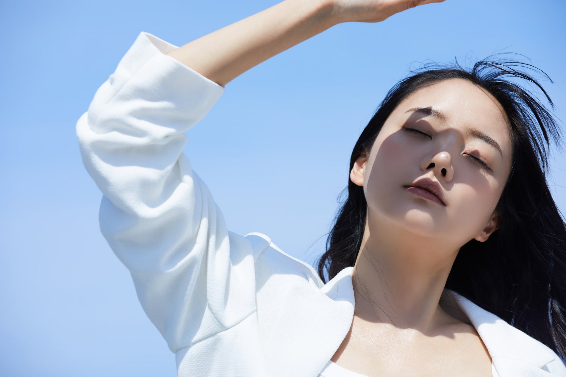 Junge asiatische Frau mit weißem Oberteil schützt sich vor der Sonne mit ihrer Hand