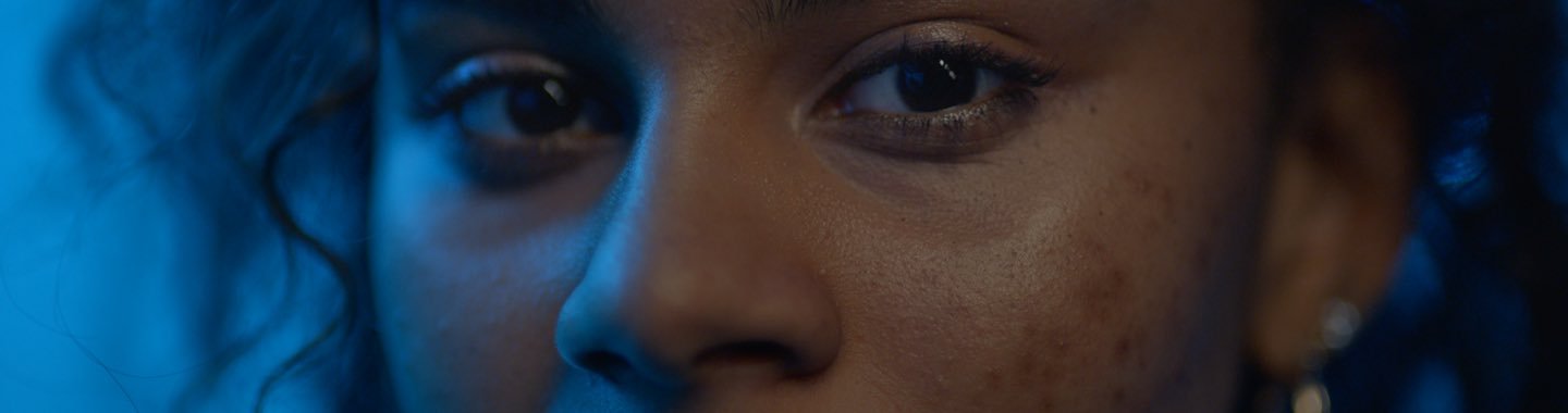 Nahaufnahme der Augenpartie einer jungen Frau mit dunklen Augen welche von links von blauem Licht beleuchtet wird