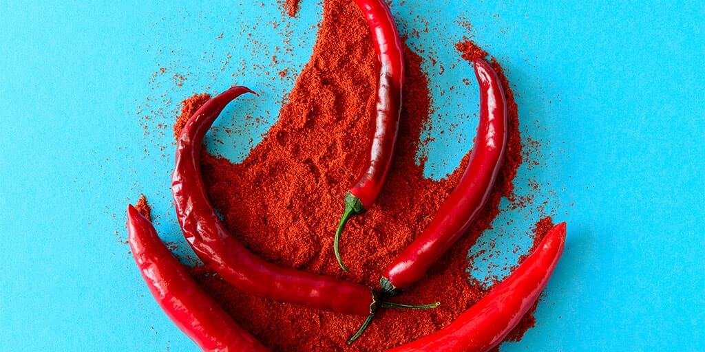 Mehrere Chili-Schoten auf Chili-Pulver in Form einer Flamme auf blauem Untergrund