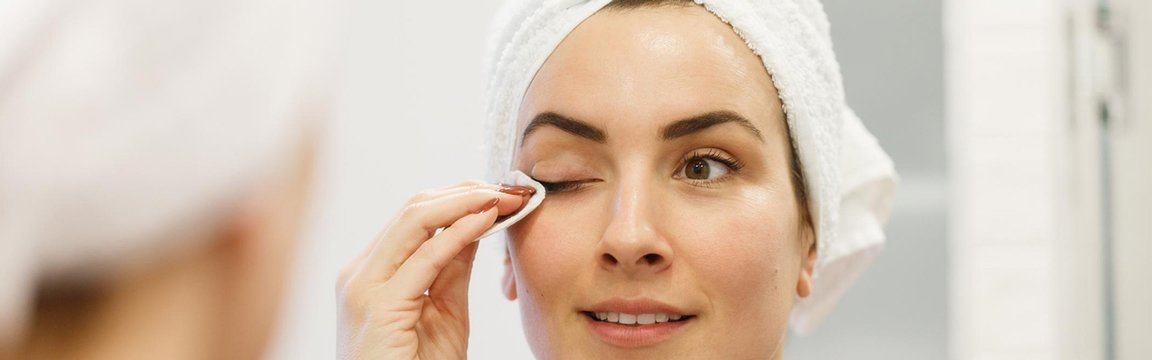 Junge Frau mit Handtuch auf dem Kopf schminkt ihre Augen ab