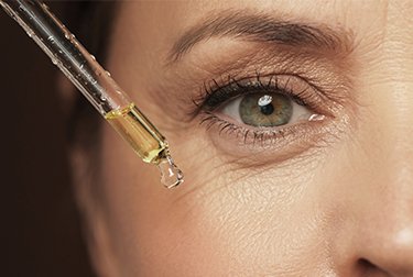 Ältere Frau mit Falten um die Augen trägt ein Anti-Aging-Serum auf