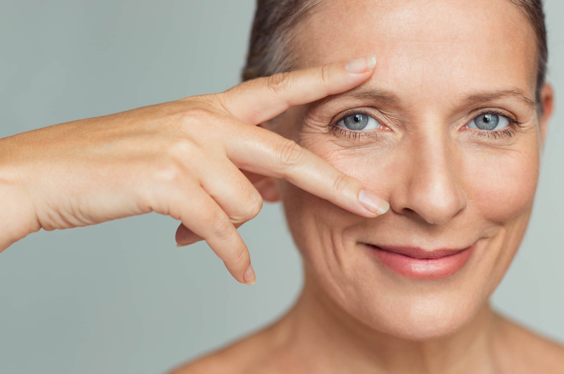 Frau mit leichten Falten um die Augen hält ihre zwei Finger ins Gesicht