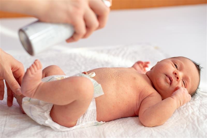 Mutter sprüht Thermalwasser auf die von Dermatitis betroffene Haut ihres Neugeborenen