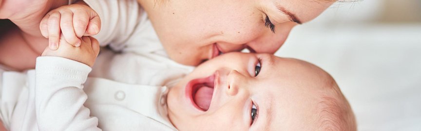Mutter gibt ihrem lachenden Baby einen Kuss auf die Wange