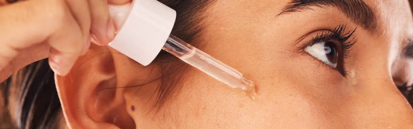 Frau tropft ein Serum auf ihr Gesicht mit Leberflecken
