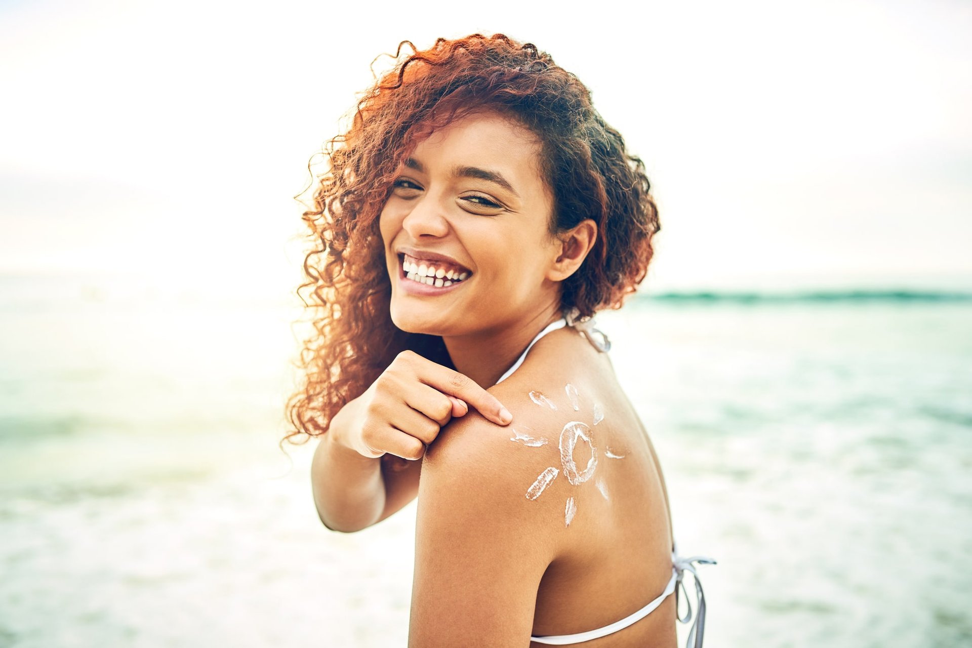 Junge Frau im Bikini cremt sich ihre Schulter in Form einer Sonne ein