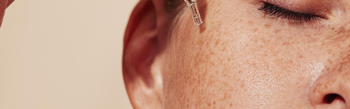 Frau mit Sommersprossen trägt sich mit einer Pipette ein Serum im Gesicht auf.