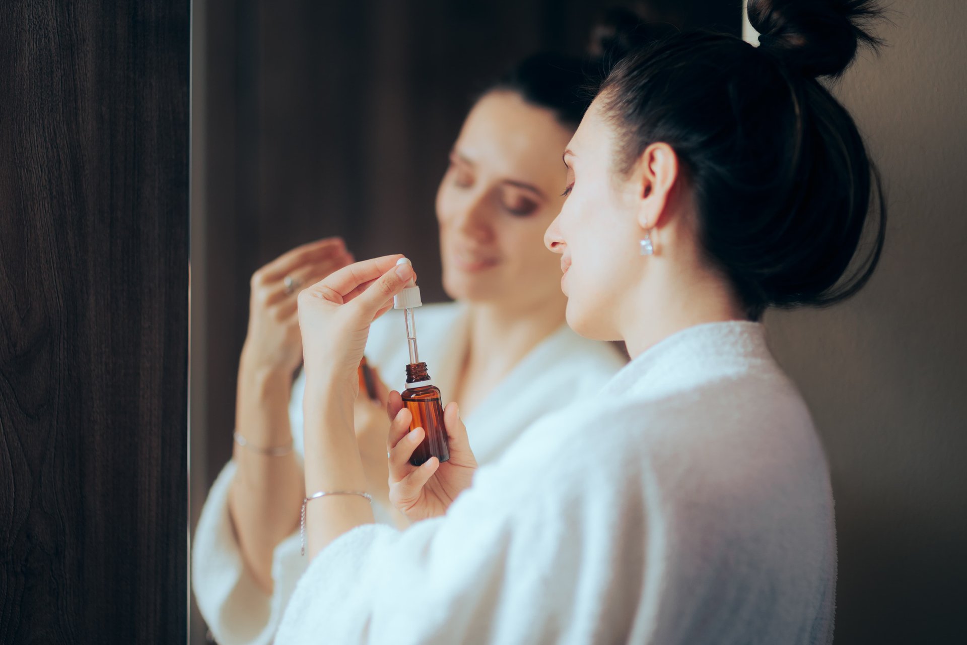 Frau hält vor dem Spiegel eine Pipettenflasche mit Retinol-Serum in der Hand 