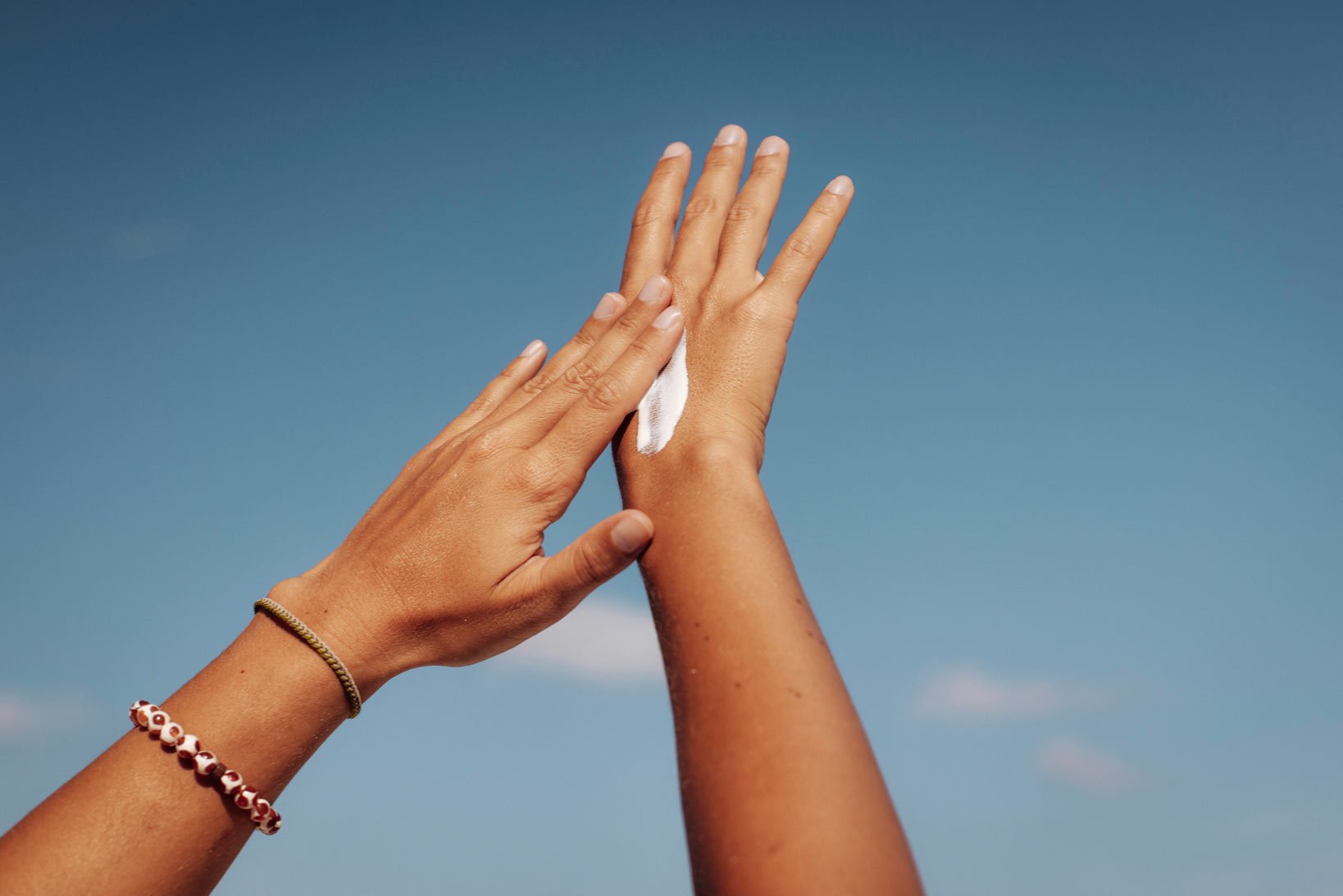Hand verteilt Sonnencreme auf dem Handrücken vor klarem blauem Himmel