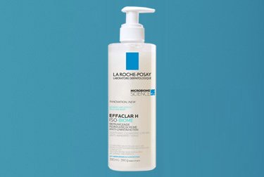 Effaclar H Iso-Biome Reinigungscreme von La Roche-Posay in weißer Pumpflasche, gehalten von einer behandschuhten Hand vor hellblauem Hintergrund.  Geben Sie Ihr Feedback zu BizChat ab.