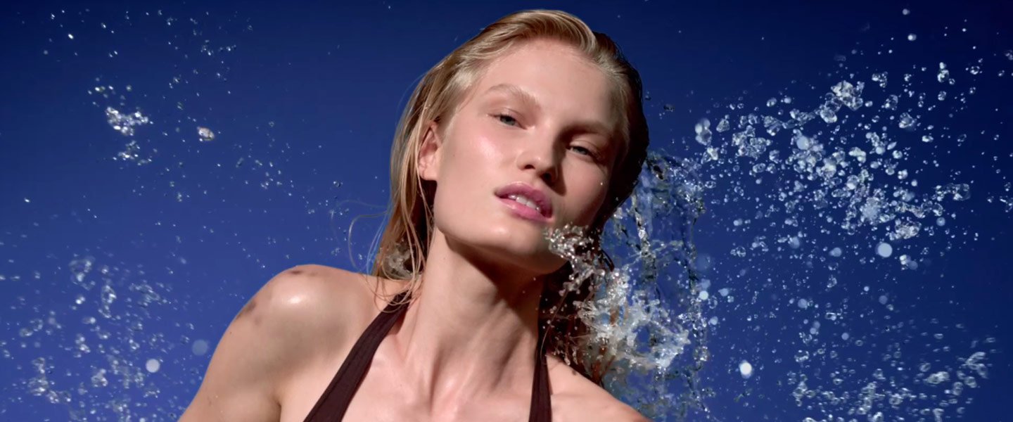 Frau mit blonden Haaren vor blauem Himmel, umgeben von spritzendem Wasser