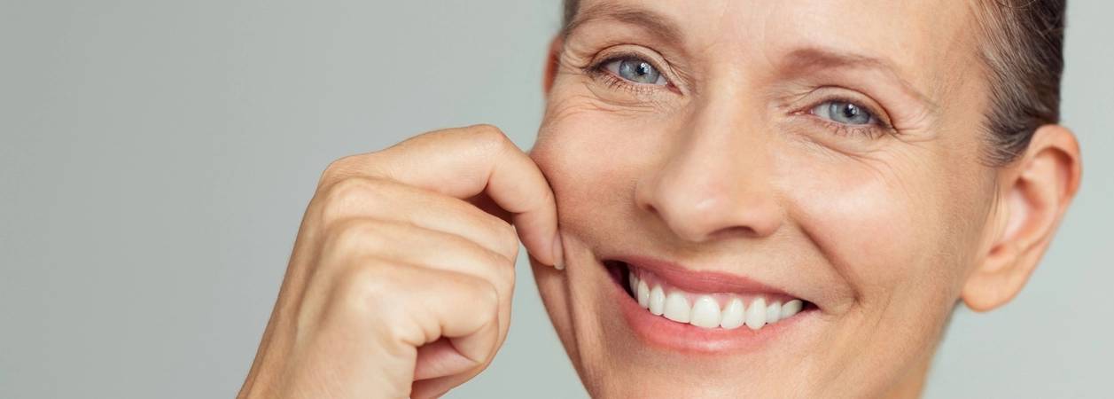 Frau zieht ihre Wange, um die Straffheit ihrere Haut zu zeigen