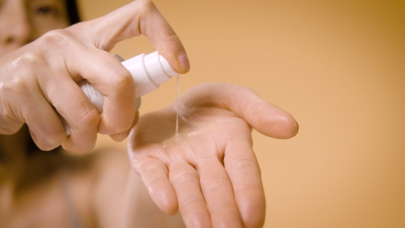 Vor einem gelben Hintergrund sieht man zwei Hände, die eine Hand lässt Gel aus einem Behälter auf die andere Laufen
