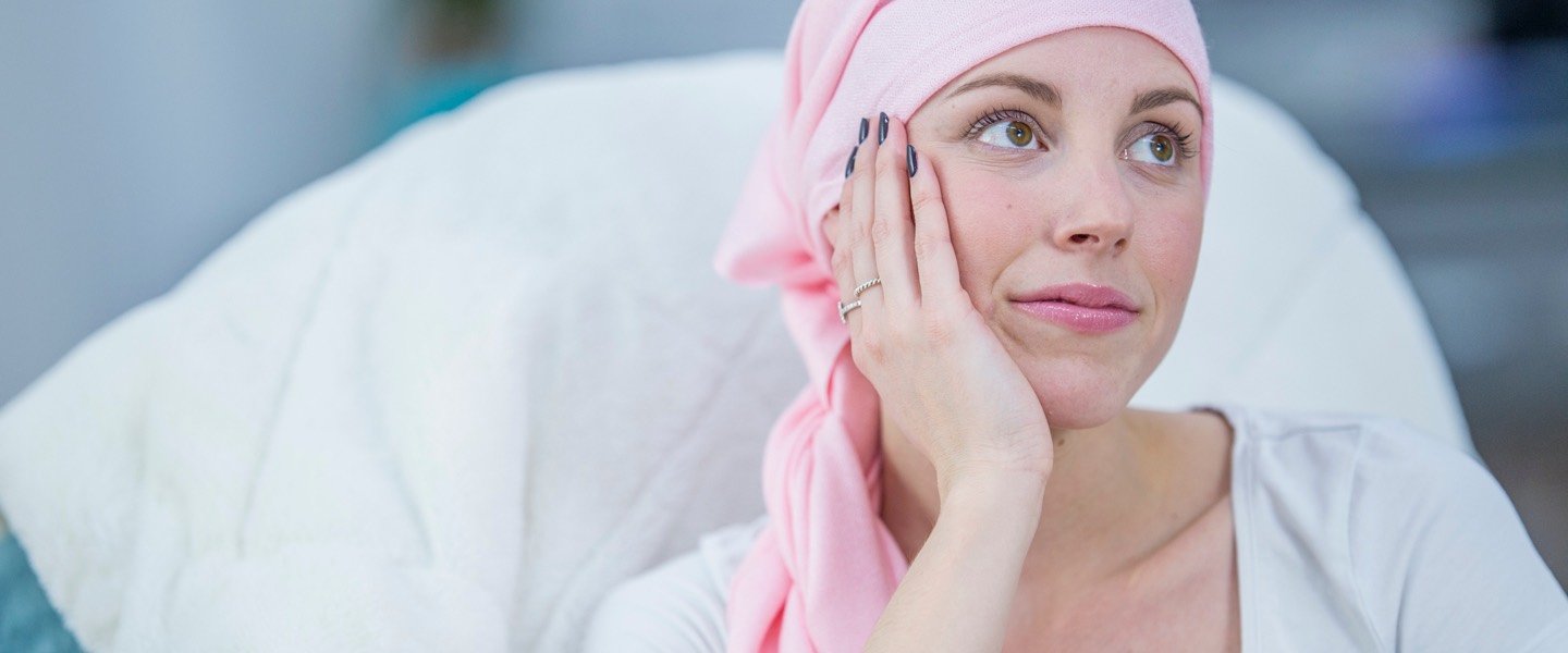 Krebspatientin mit rosa Tuch um den Kopf stützt ihr Gesicht mit ihrer Hand