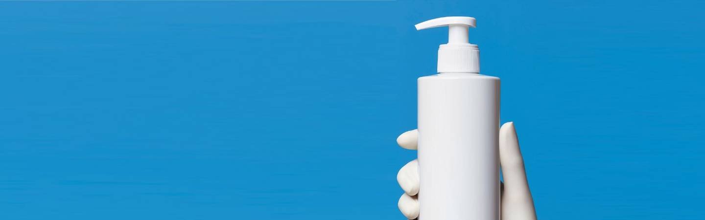 Hand in weißem Gummihandschuh hält einen weißen Pumpspender