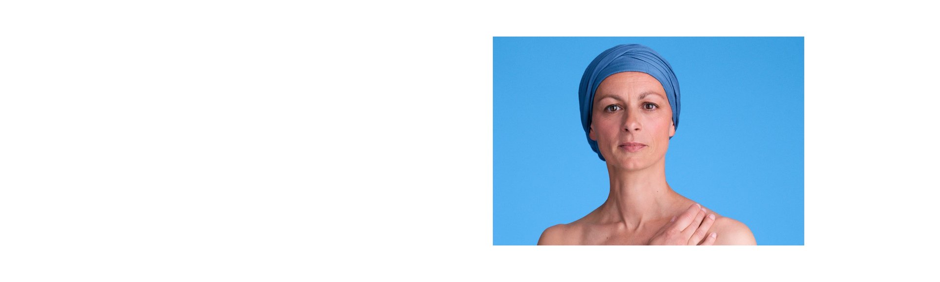 Eine an krebs erkrankte Frau mit bleuen Turban steht vor einem blauen Hintergrund