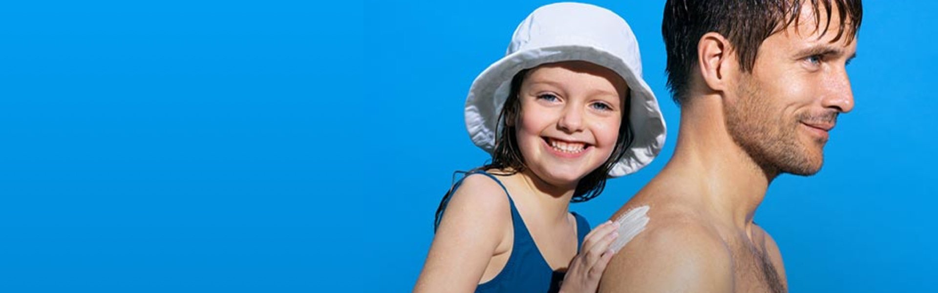 Eine Person trägt Sonnencreme auf die Schulter einer anderen Person auf, vor blauem Hintergrund mit sommerlichen Accessoires.